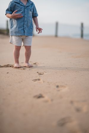 Close-up view of bare feet walking in soft sand on a beach with blurred denim clothing visible in background.