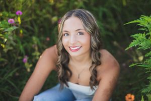 Portrait session showing subject in a navy top against vibrant garden foliage with pink flowers.