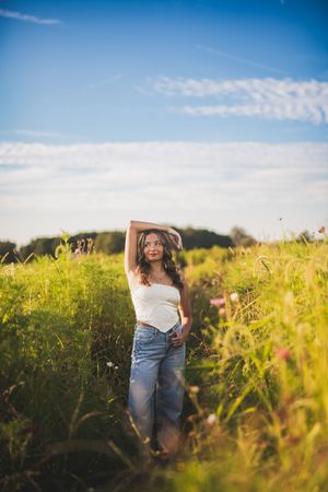 Woman in denim and white top walks through golden wildflower field on sunny summer day.