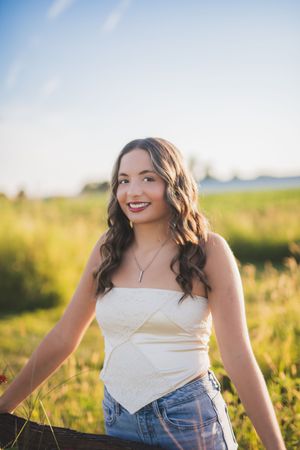Summer outdoor portrait of a figure in a white top and denim, photographed in golden hour sunlight.