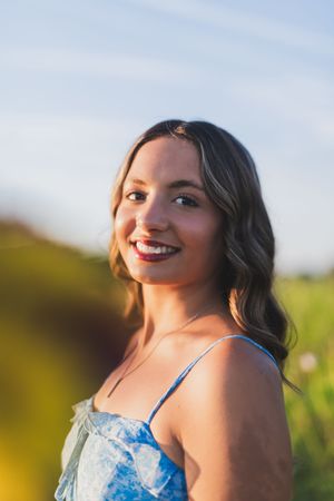A woman in a sparkly blue formal dress poses in a sunlit field during golden hour.