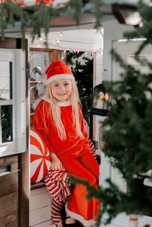 A festive holiday scene with red and white striped decor and evergreen branches framing a cozy porch setting.