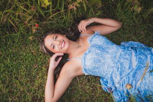 Someone wearing a blue floral dress lies peacefully on lush green grass surrounded by blooming flowers and foliage.