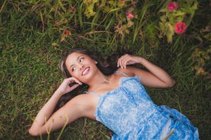 Person in blue patterned dress relaxes on green grass with scattered flowers in an outdoor garden setting.