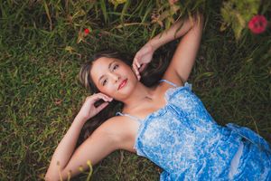 Woman in blue lace dress poses gracefully among flowering plants in natural outdoor setting.