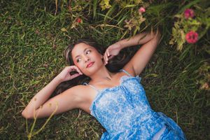 Woman in blue dress lying in grass field with flowers on sunny afternoon.
