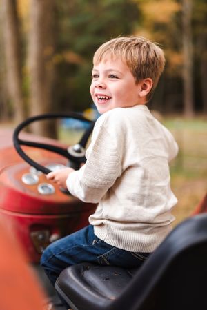 Child sitting on vintage red tractor with joyful expression.