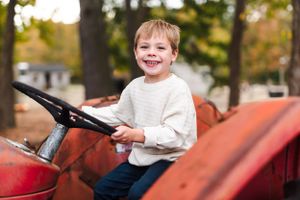Child joyfully steering red tractor in fall outdoor setting.