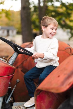 A child giggles while playing on an old red tractor on an autumn day.