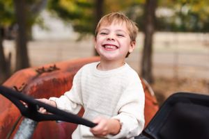 Child laughing while steering vintage red tractor in outdoor setting.