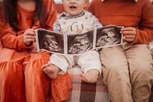 People wearing matching orange shirts sit together while holding black and white ultrasound photos.