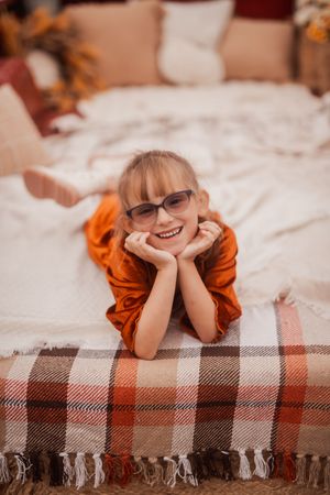 A playful pose on a plaid blanket wearing an orange knit top while smiling at the camera.
