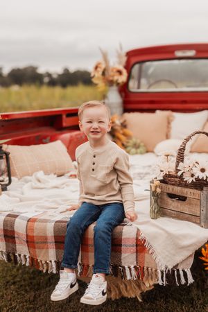 A vintage red pickup truck bed decorated with cozy plaid blankets and throw pillows creates a rustic autumn scene.