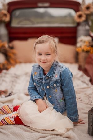 A young child in a denim jacket lies on white textured fabric while looking at the camera.