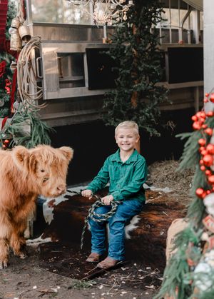 A golden retriever and companion sit together on a porch decorated with festive holiday greenery and red berries.