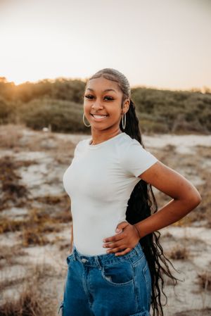 Young woman in white shirt and jeans poses outdoors at sunset with long braided hair.