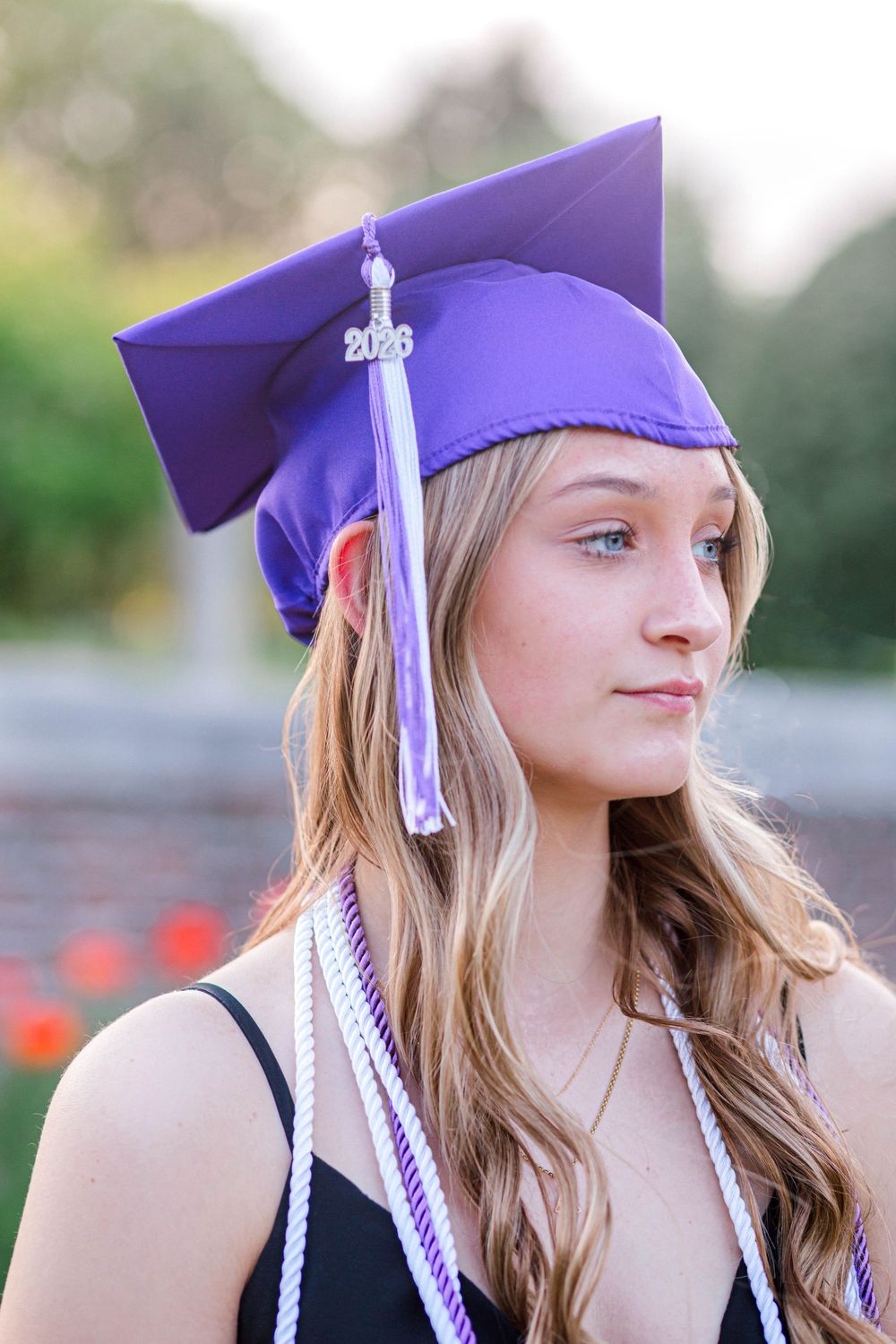 Young woman in purple graduation cap with 2023 tassel and honor cords, smiling outdoors at graduation ceremony.