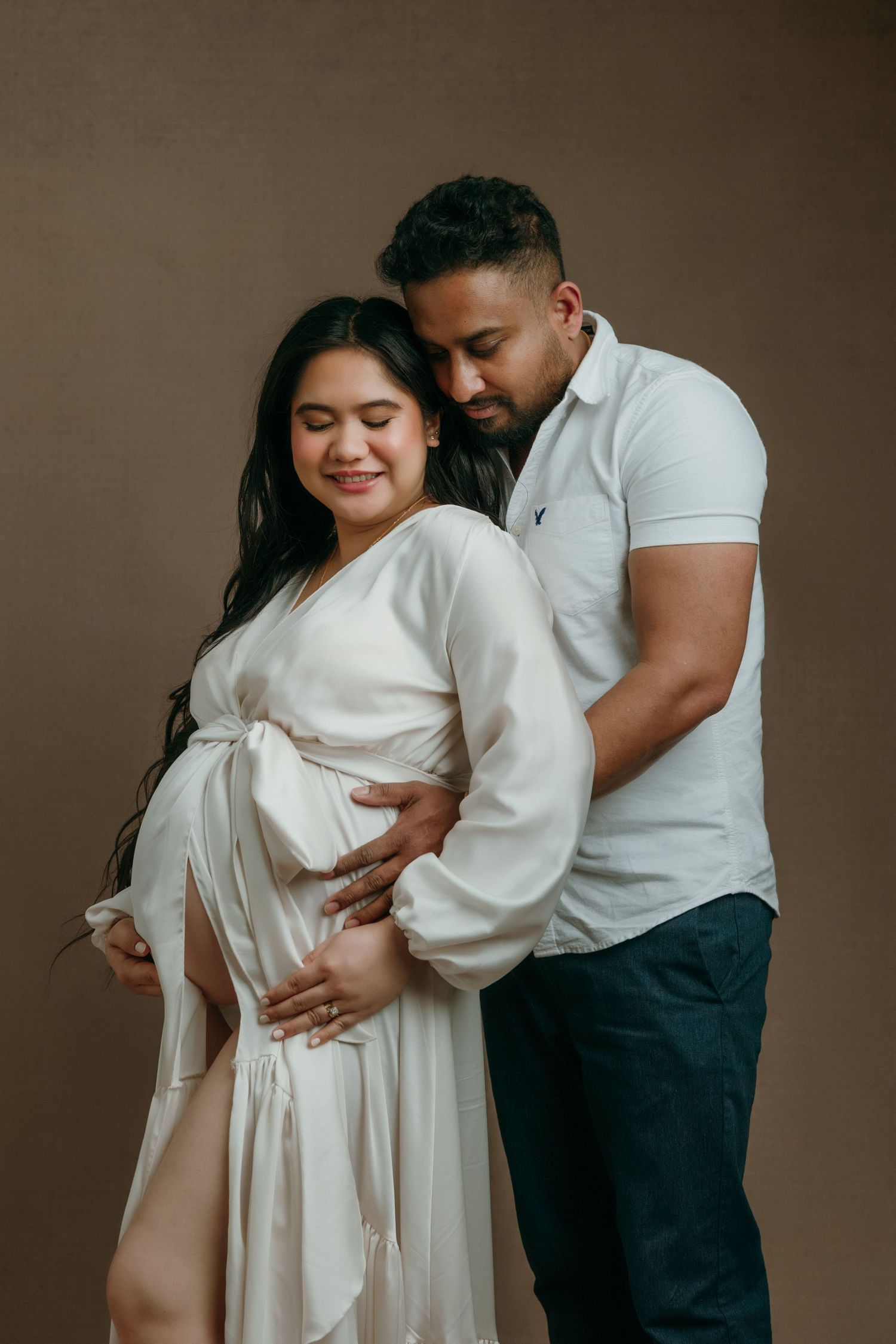 A pregnant woman in a white robe poses with her partner in a tender maternity studio portrait Victoria BC.
