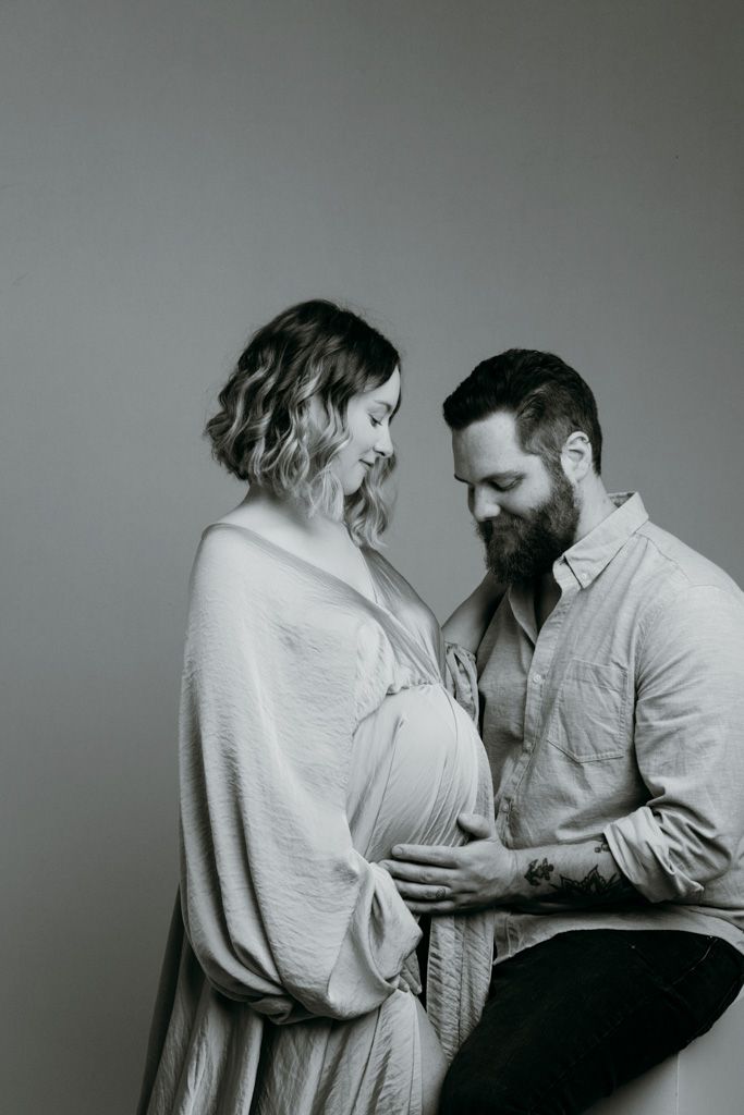 A black and white intimate maternity portrait shows an expectant couple sharing a tender moment together at the studio in victoria bc.