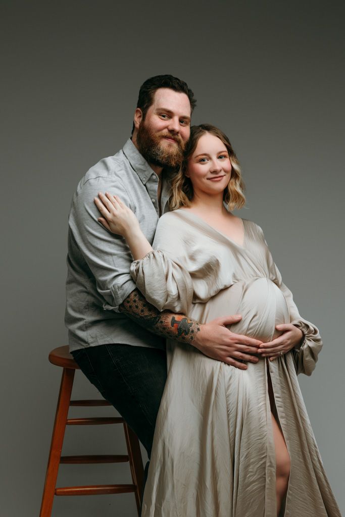 Intimate maternity photo series showing couple embracing in cream colored outfits against neutral backdrop at the studio in victoria bc.