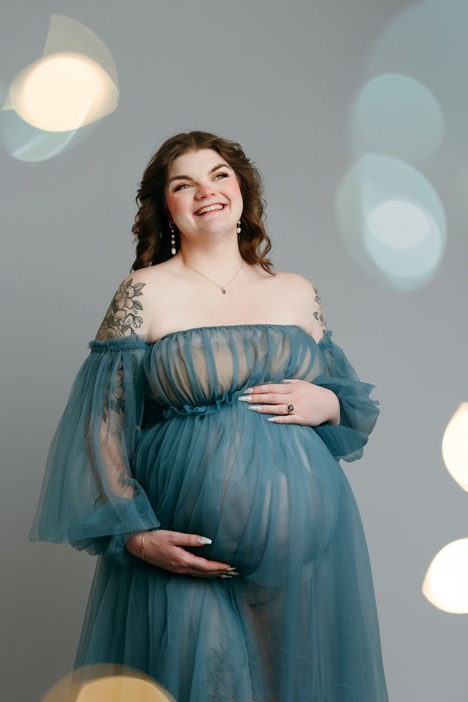 Maternity portraits featuring expectant mother in flowing blue tulle gown with bokeh light effects taken at the studio in victoria bc.