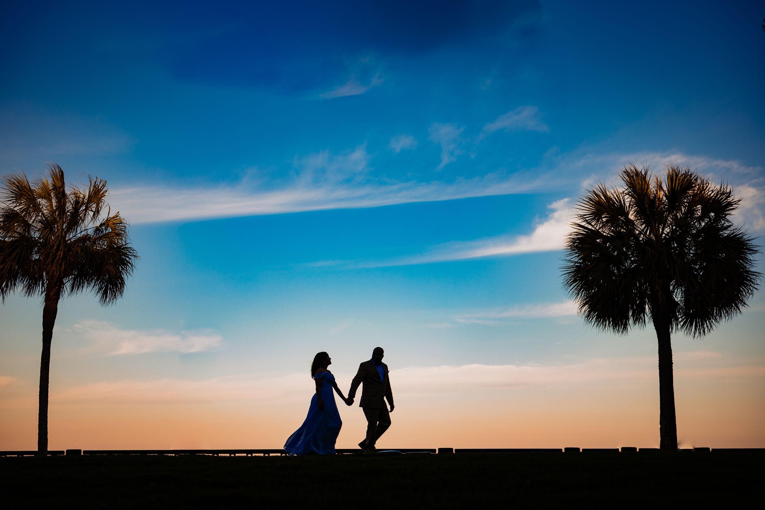 Silhouette of a couple holding hands at sunset between two palm trees. Charleston SC