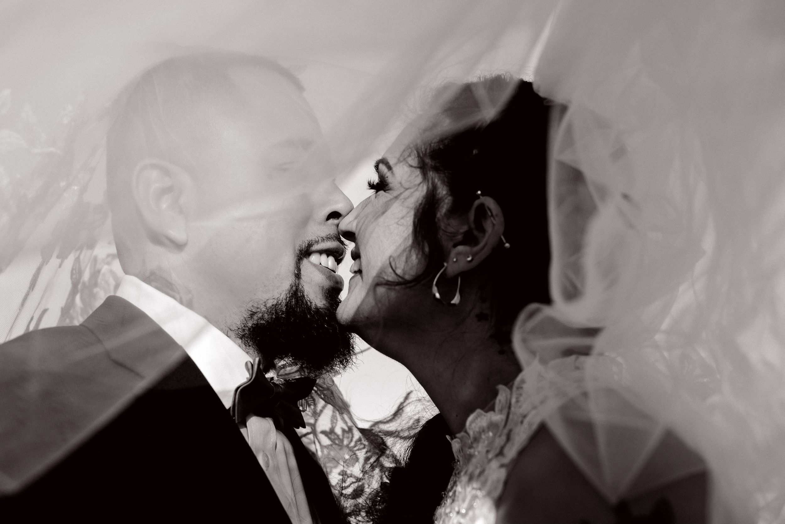A romantic black and white wedding photograph showing a couple sharing a tender moment under a flowing veil. Summerville/Charleston, SC