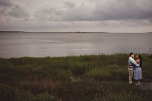 Couple embracing near lush green marsh grass with calm water and dramatic cloudy sky in background.
Summerville/Charleston, SC