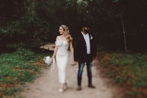 A bride in a white midi dress and groom in a black jacket walk hand in hand along a forest path.
Summerville/Charleston, SC