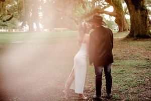 Couple sharing a romantic kiss under oak trees in golden sunlight, bride in white dress and groom in hat. Summerville/Charleston, SC