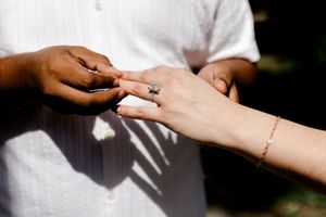 Close-up of an interracial couple exchanging rings during a wedding ceremony outdoors in sunlight. Summerville/Charleston, SC