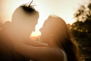 A silhouetted couple embraces in front of a golden sunset with streaming sunlight creating a romantic backlit effect.