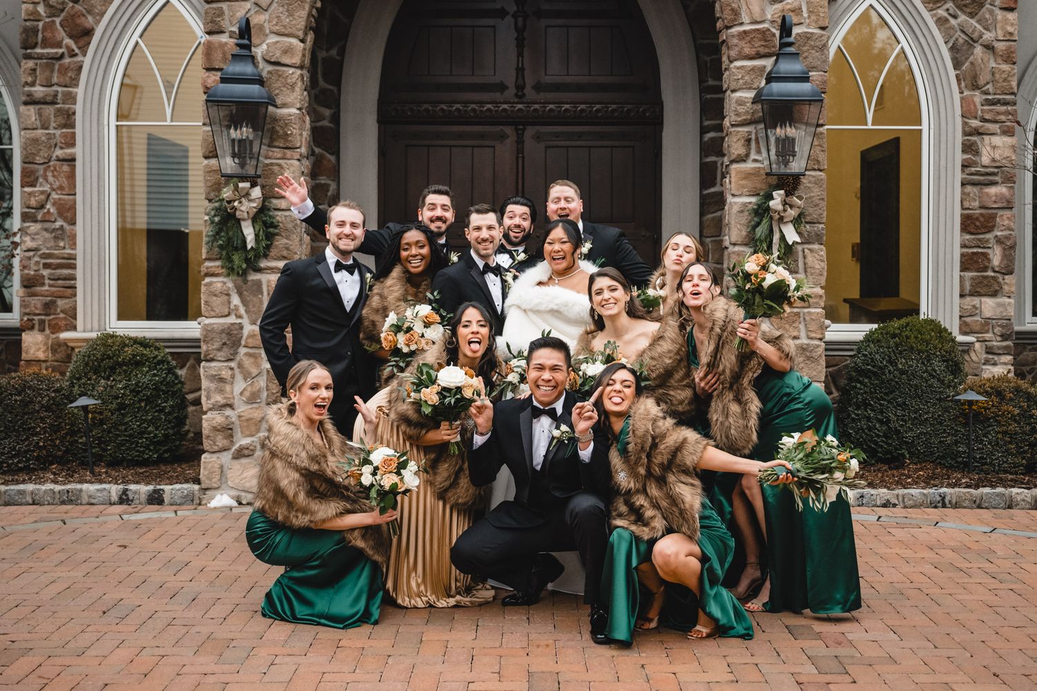 Wedding party poses together in front of stone church with Gothic arched doorway and emerald green bridesmaids dresses.