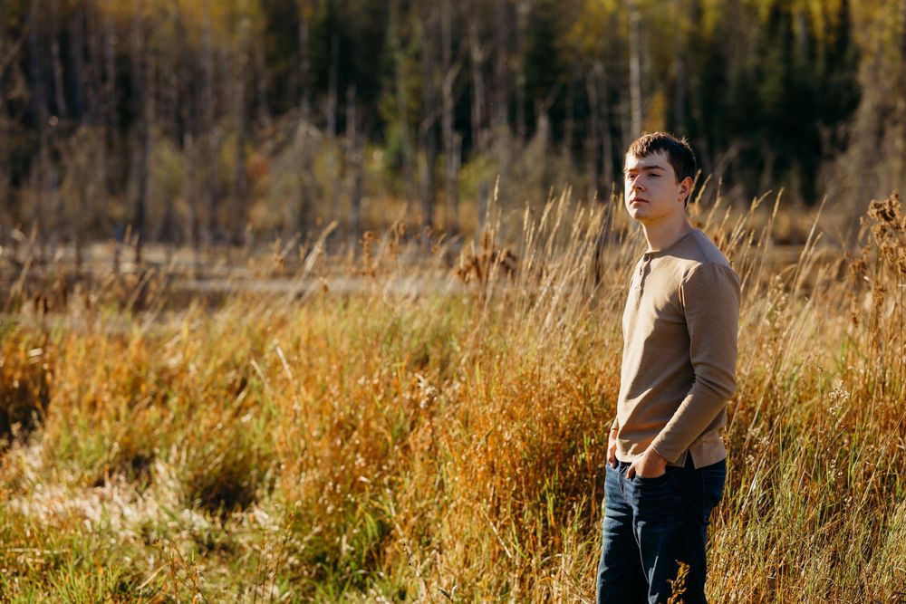 Gunner posing for senior photo in grassy field northern midwest