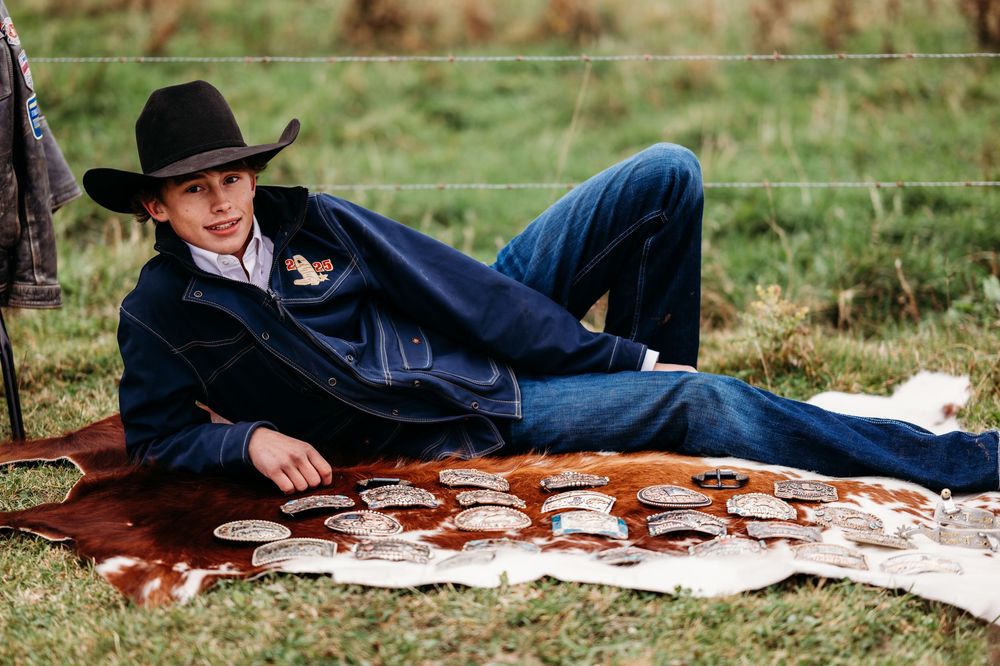 cowboy with black hat posing with championship belt buckles
