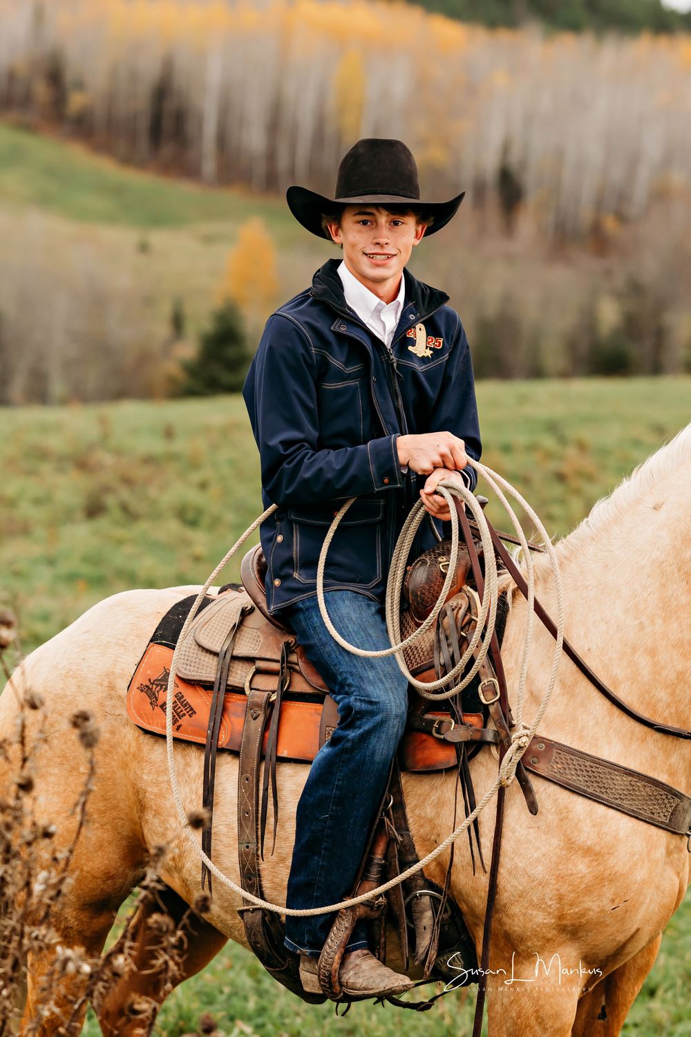 sideview of cowboy with rope and black hat on tan horse in a field