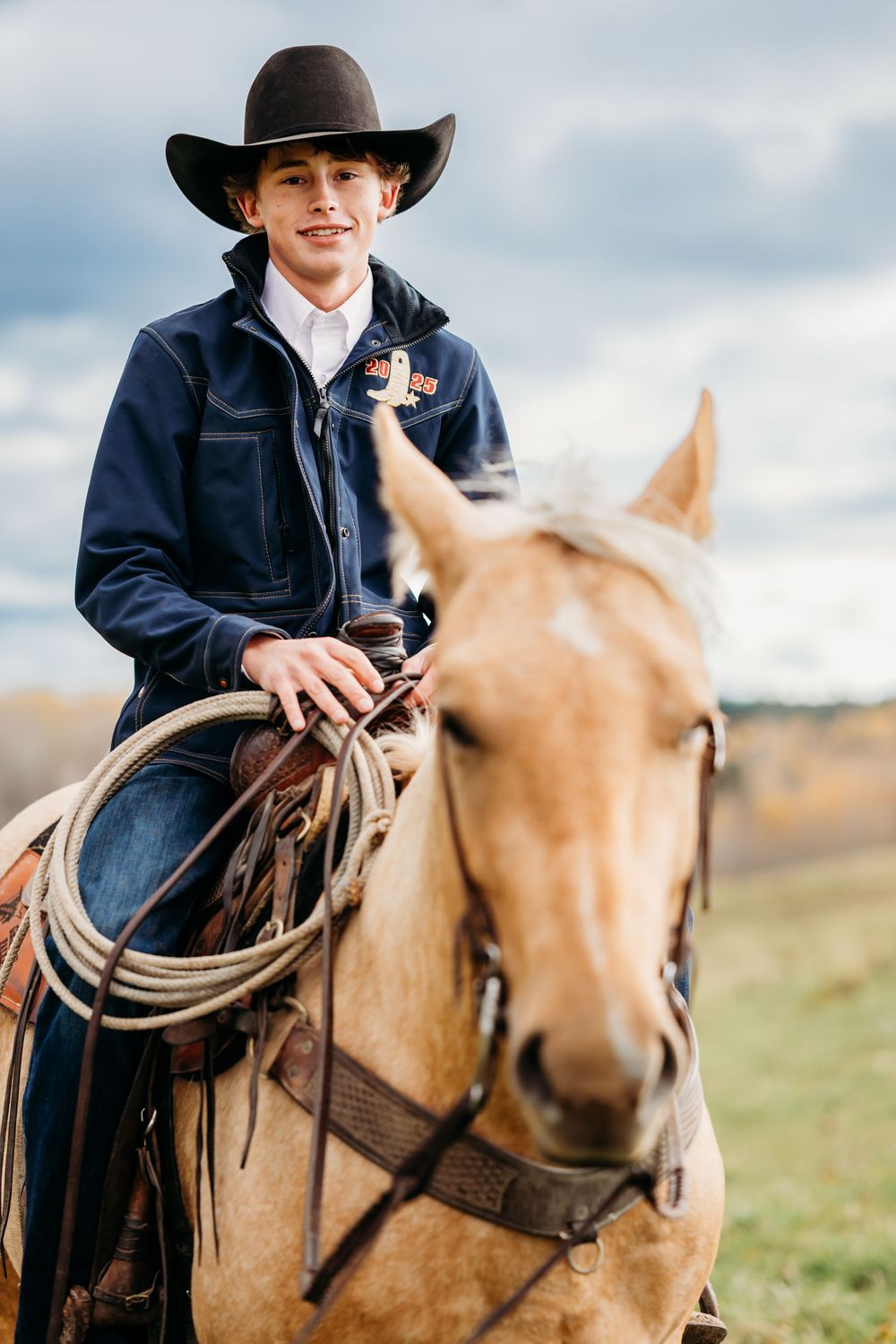 Cowboy on tan horse in a field posing for senior photosession