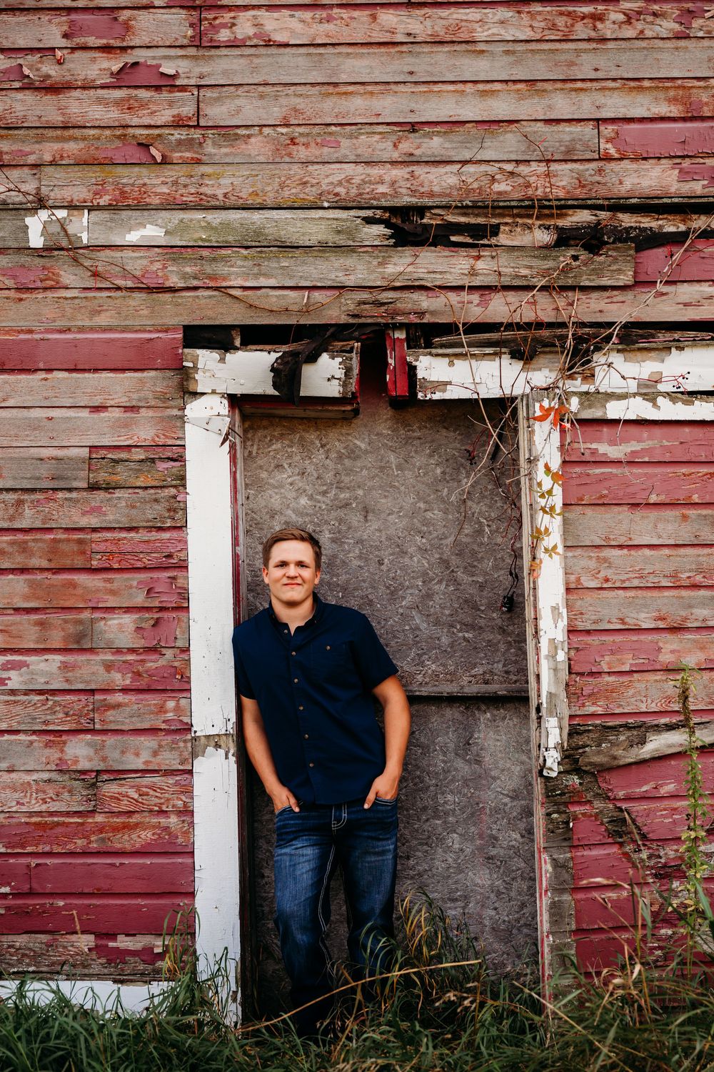 Jaxin standing in doorway against red barn senior photography