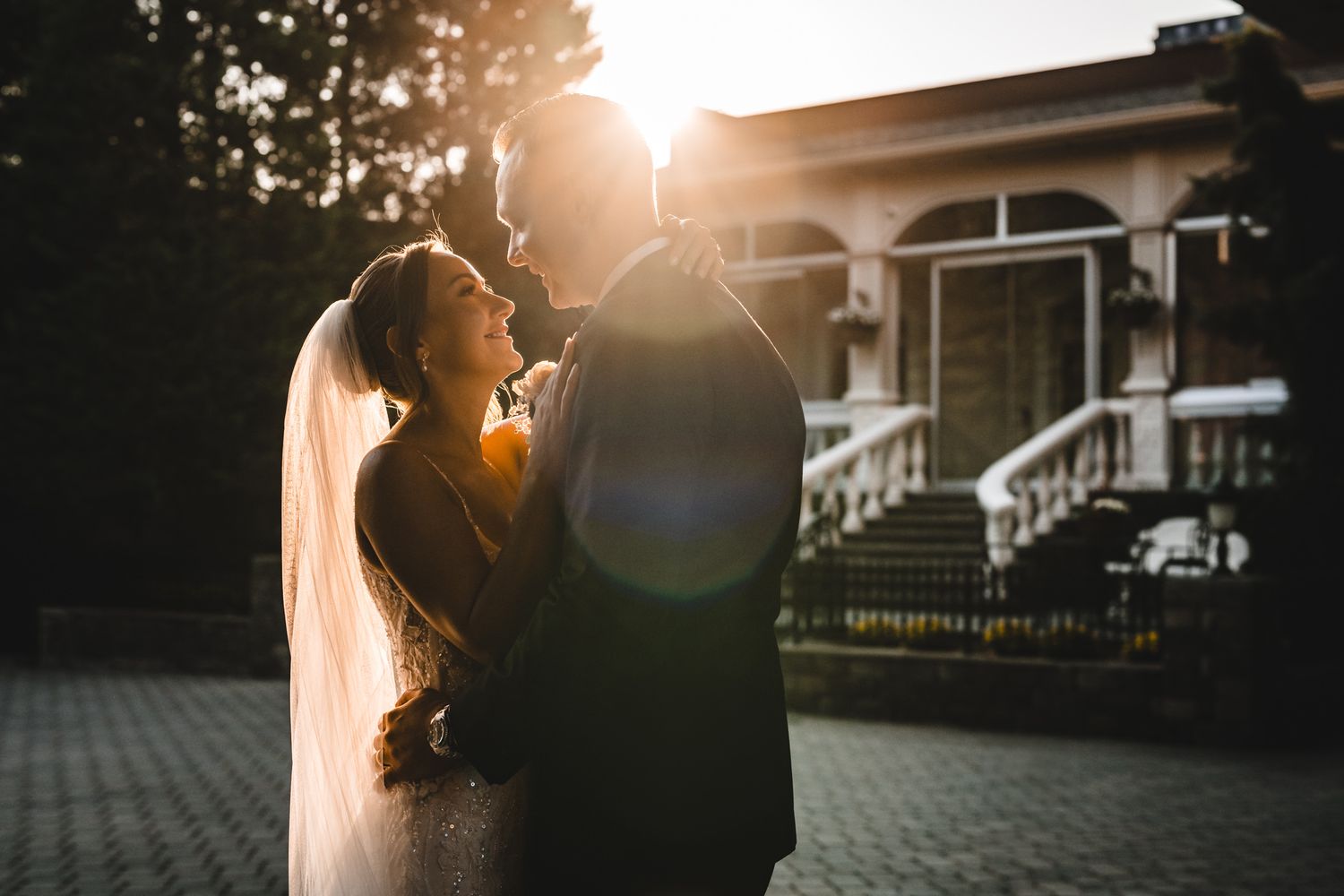 Silhouetted couple embraces in romantic sunset light with lens flare against architectural backdrop.