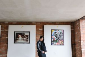 A person stands against an exposed brick wall with two framed artworks, wearing dark casual clothing.