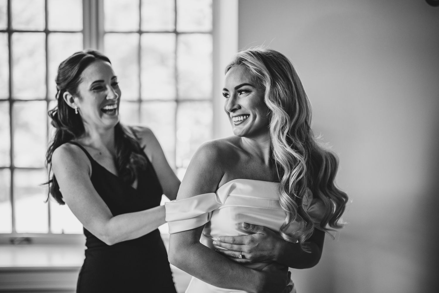Black and white candid moment of joy and laughter during wedding preparations.