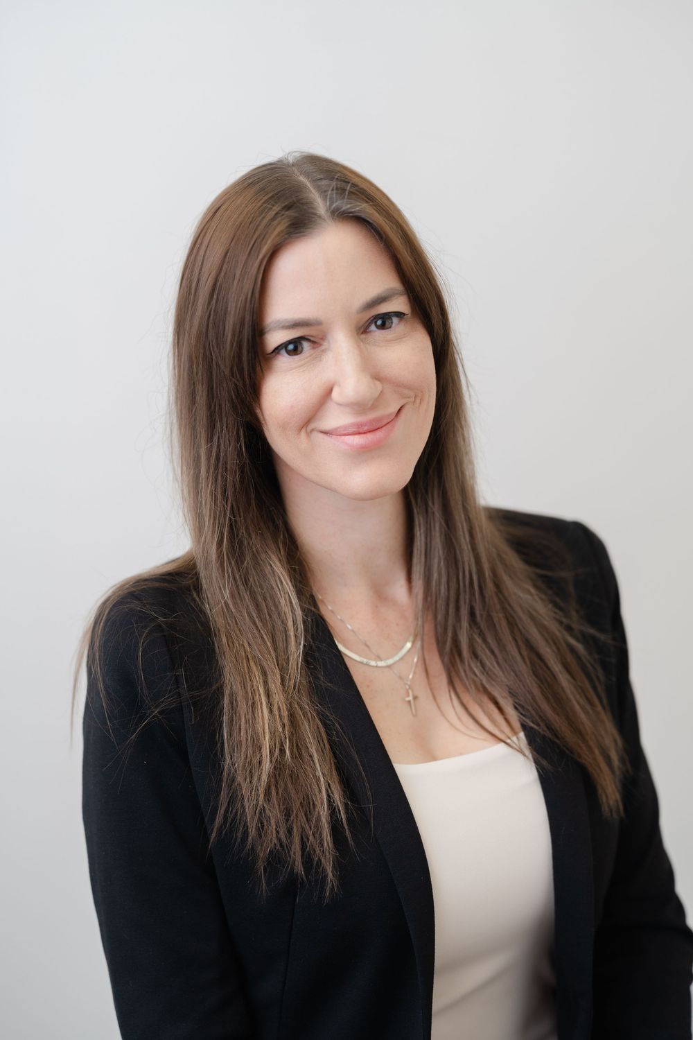 Professional headshot of a woman with long brown hair wearing a black blazer and delicate necklace.