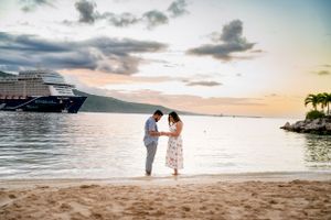 A romantic beach sunset with a cruise ship anchored in the distance and palm trees along the shore.
