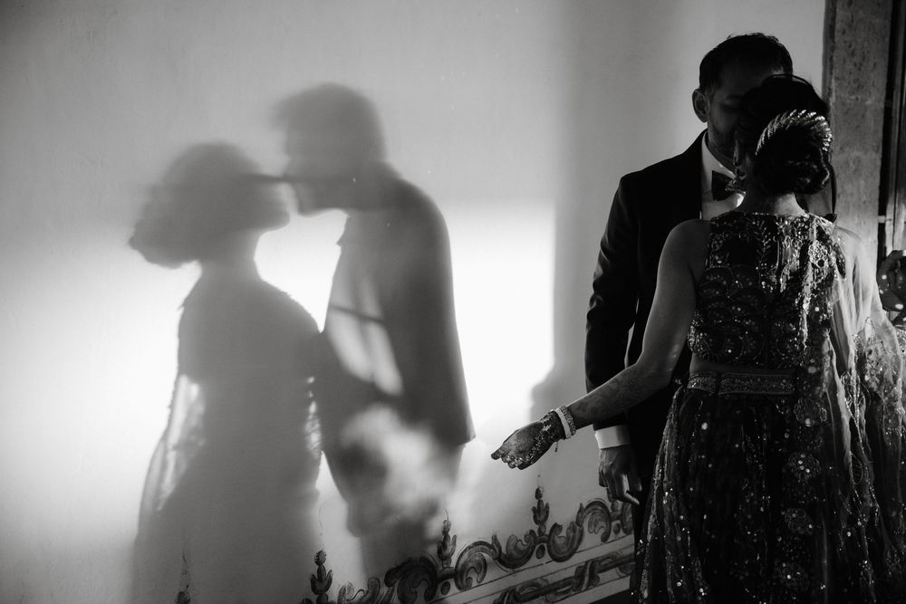 Black and white wedding photo of couple sharing romantic moment with dramatic shadow on wall.