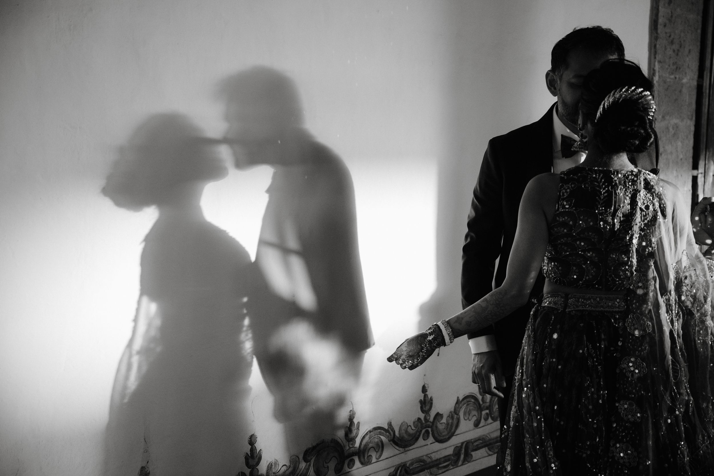 Black and white wedding photo of couple sharing romantic moment with dramatic shadow on wall.