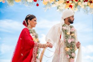 Traditional Indian wedding ceremony with couple in red and white attire under floral mandap.