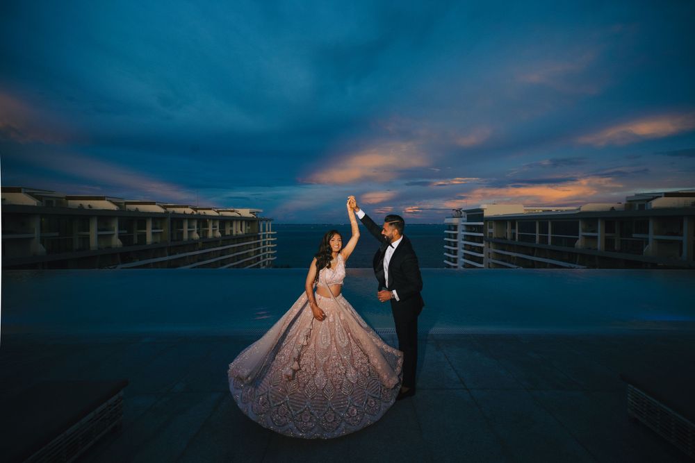 Couple in formal attire poses dramatically against dark blue sunset sky on rooftop.