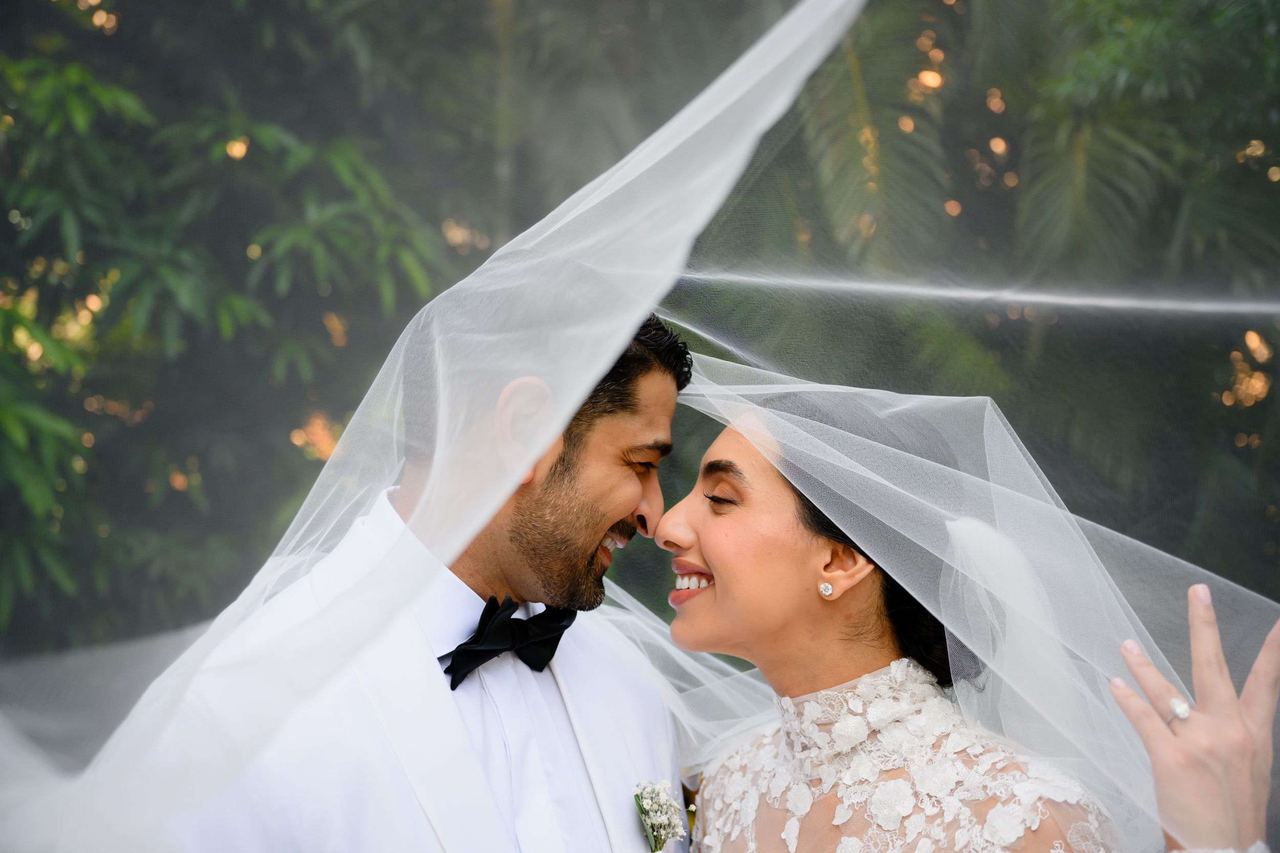 Romantic wedding portrait with couple sharing intimate moment under flowing white veil.