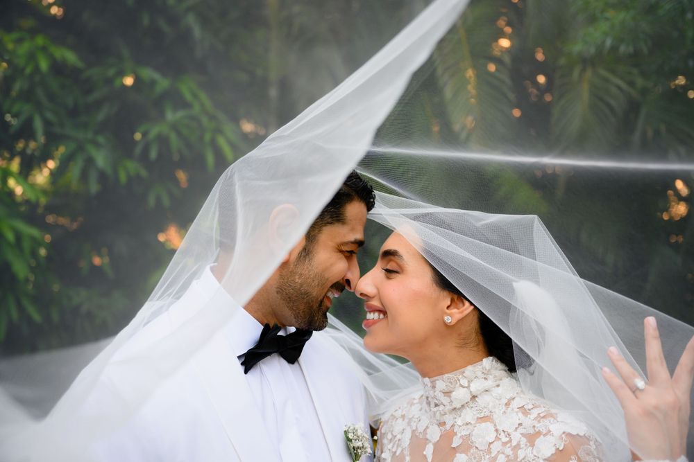 Romantic wedding portrait with couple sharing intimate moment under flowing white veil.