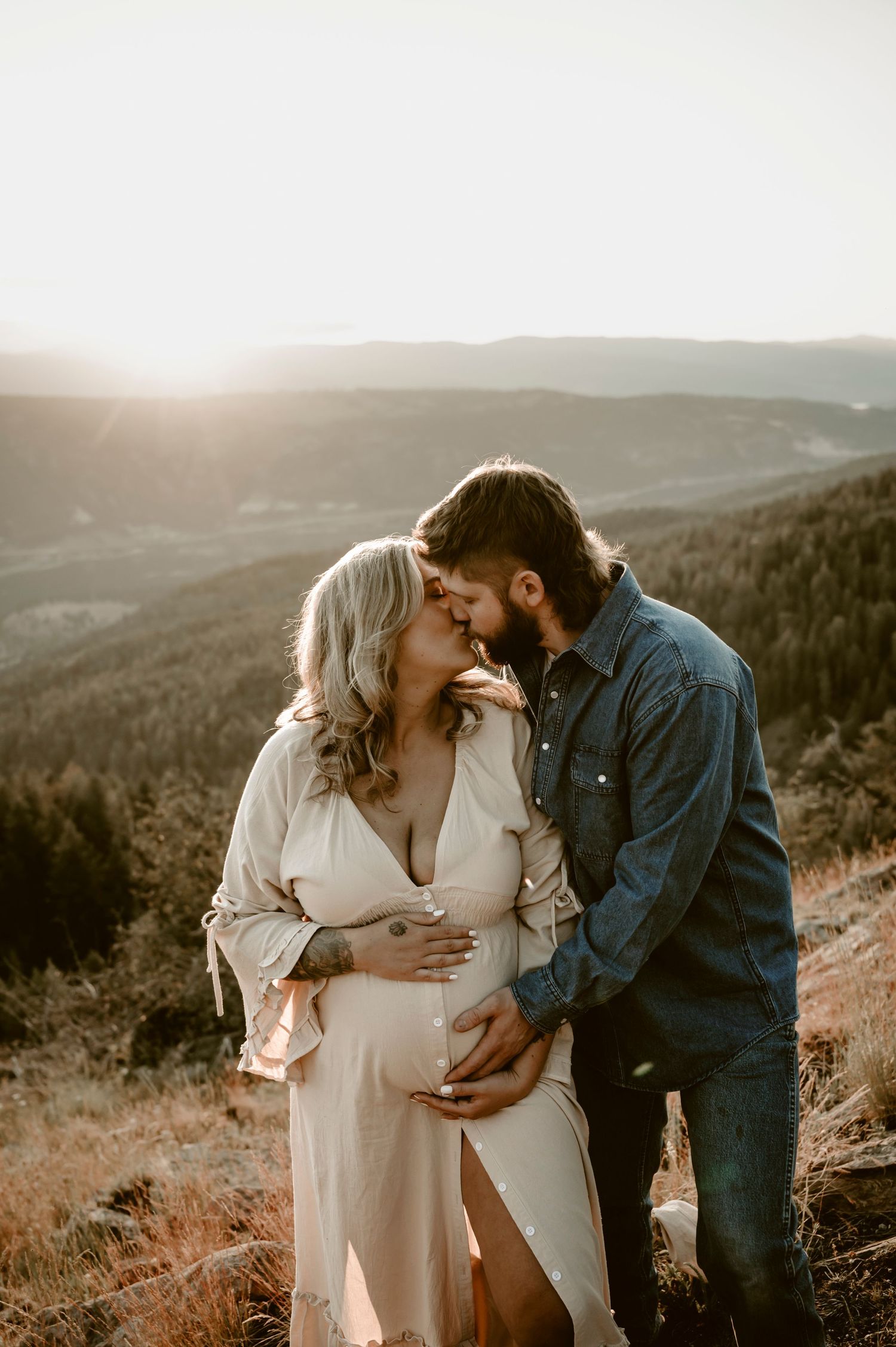 Intimate maternity photo of couple embracing on mountainside at sunset.